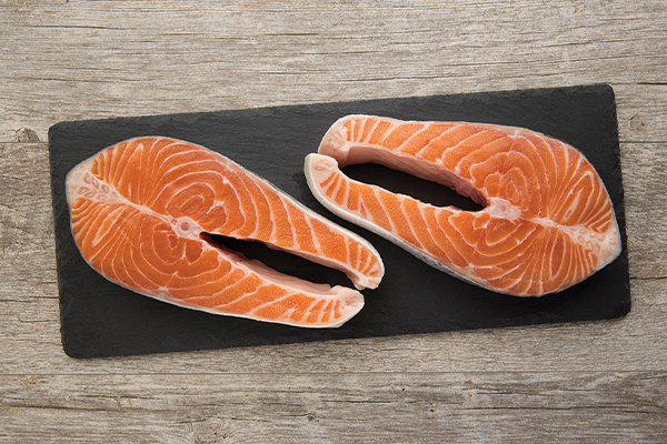 Two fresh raw salmon steaks on a black slate board.